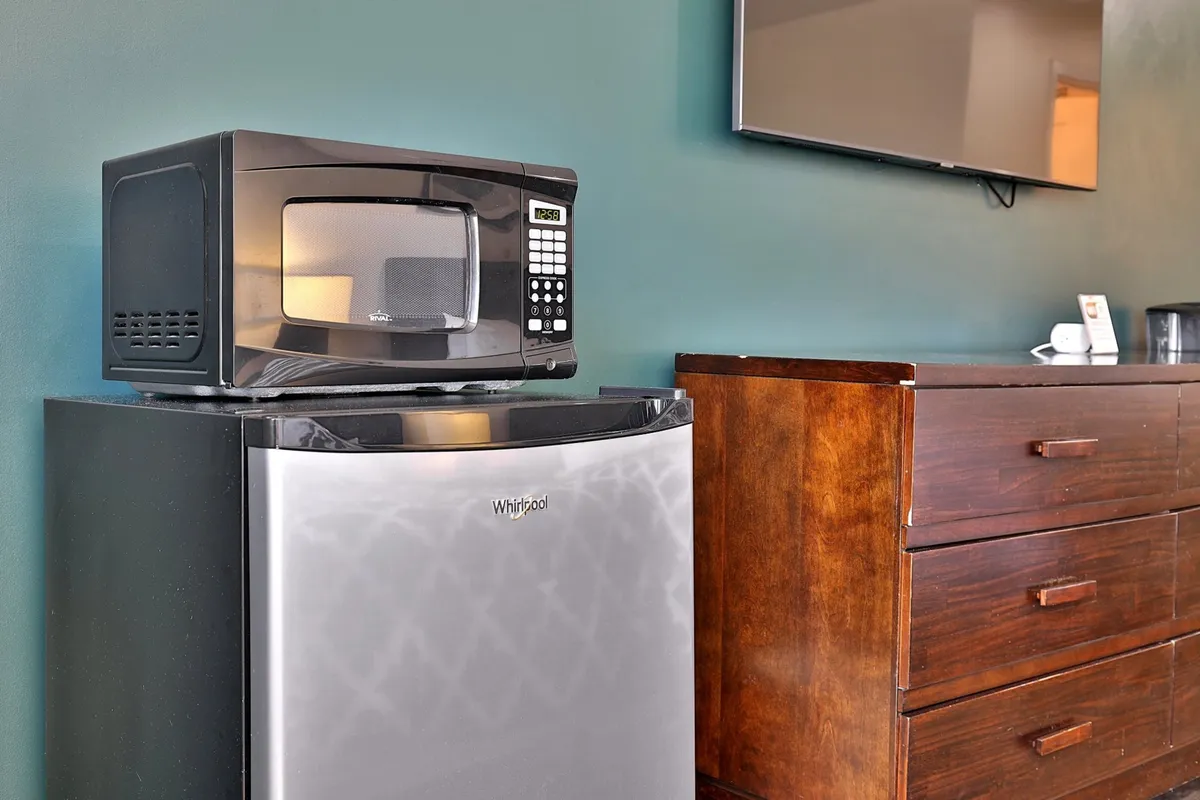 A functional kitchenette area showcasing a microwave, mini refrigerator, wooden dresser, and a wall-mounted TV. The scene suggests casual snacking, storing drinks and food, and gathering for a movie night after exploring local nightlife.