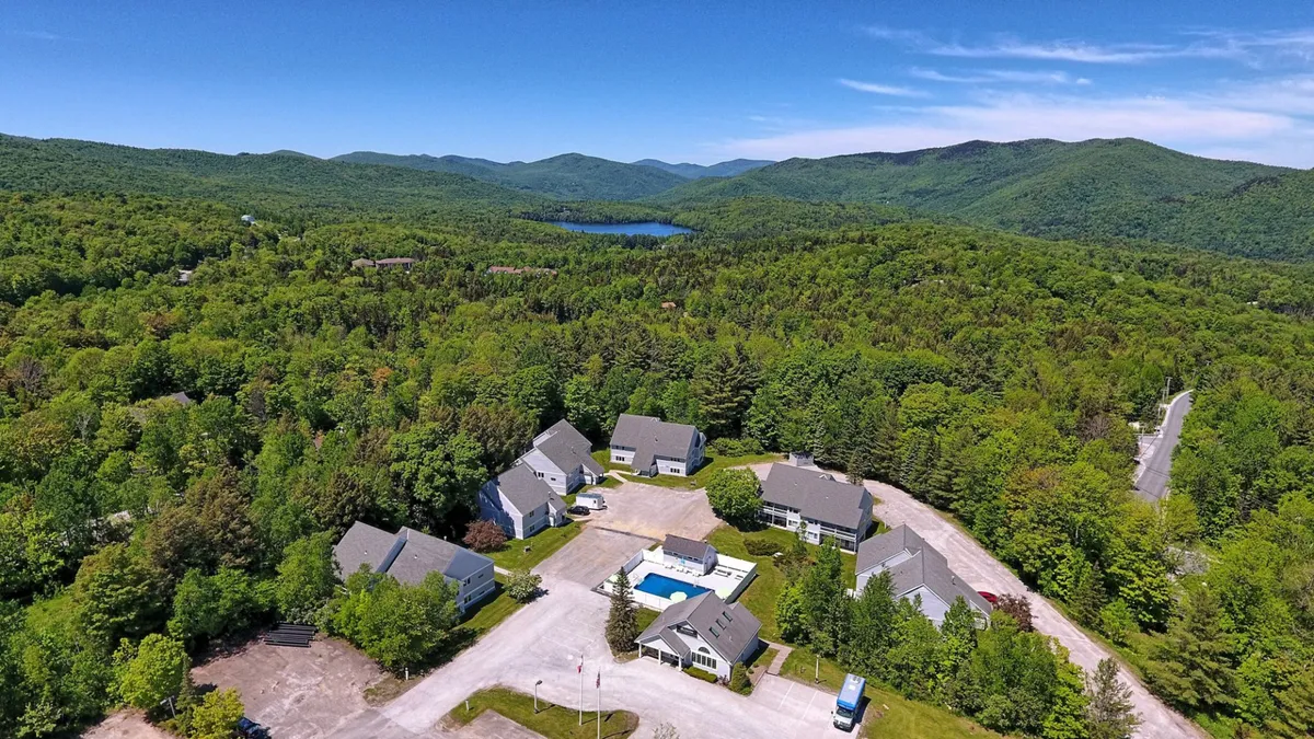 A peaceful exterior shot features the swimming pool set against a backdrop of mountains and a cluster of resort buildings. The scene captures the pool’s integration with beautiful natural surroundings—ideal for both summer leisure and winter access points.