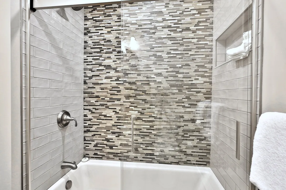 A serene ensuite bathroom featuring a modern glass shower, textured mosaic wall, and mounted towel rack. The ambiance is spa-like, with soft lighting and inviting finishes that highlight the bathroom’s modern amenities.