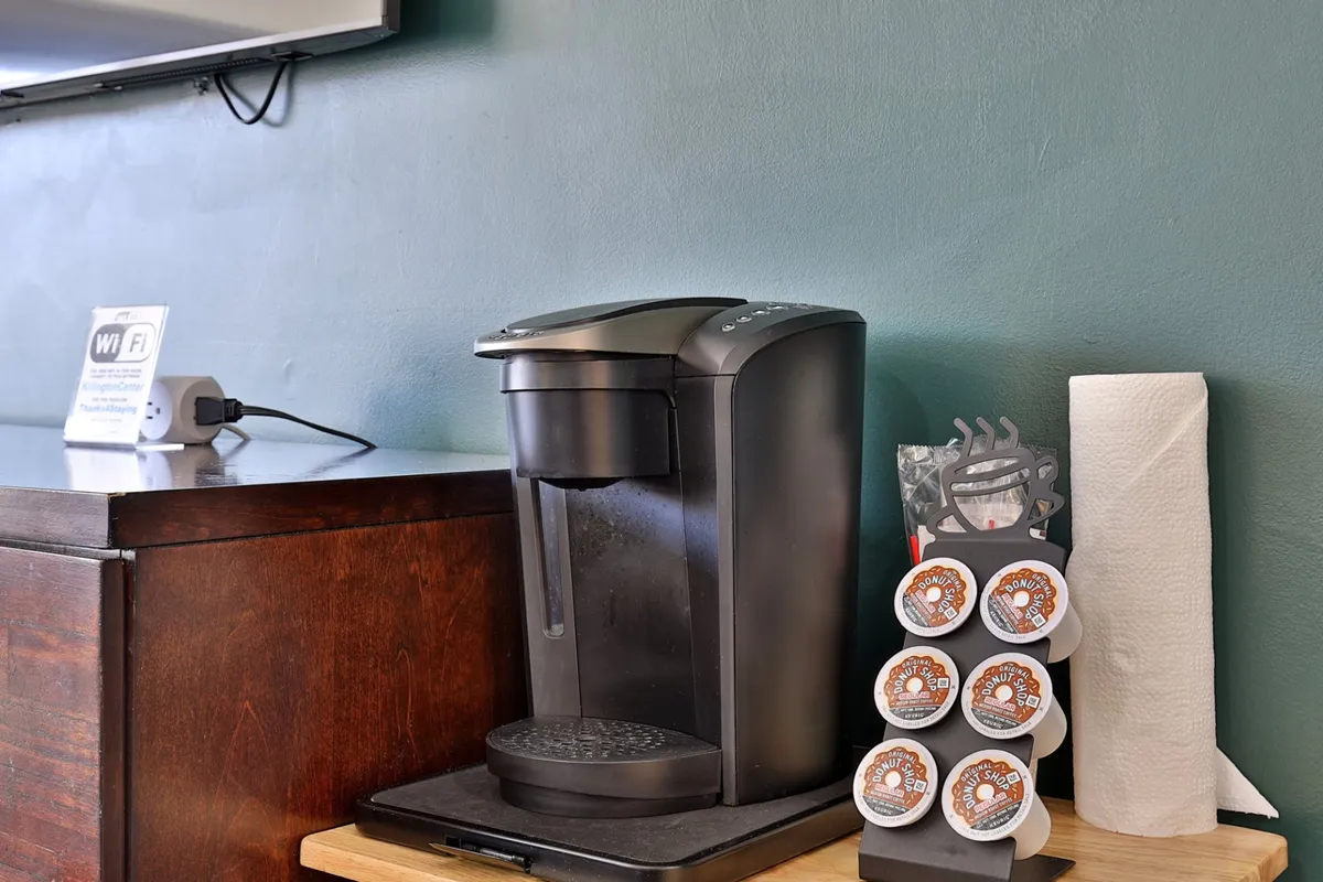 A close-up of the coffee station, including a coffee maker, pods, and paper towel holder set against a clean countertop. The setup promises simple morning rituals and adds a warm, personal touch to the studio.