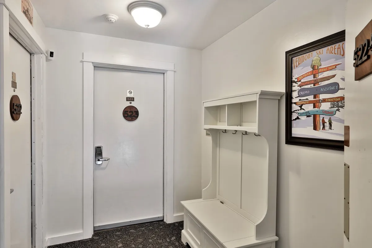 A welcoming entry area featuring a door with the number 325, a coat rack for hanging up gear, and wall art depicting ski areas. The scene evokes the moment of arrival and sets a cozy, organized tone for guests.
