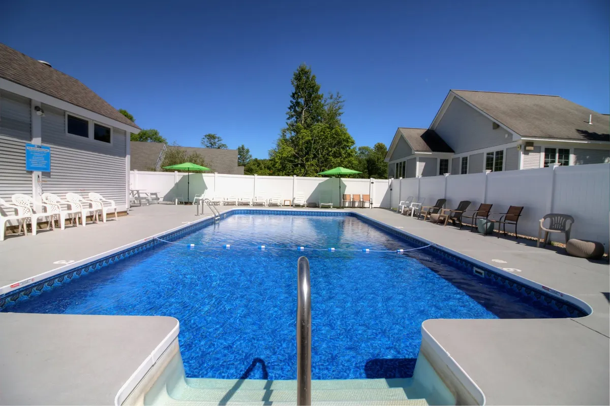 A vibrant outdoor swimming pool scene featuring poolside chairs lined up under green umbrellas. The atmosphere is lively yet relaxed, inviting for group gatherings or unwinding after a night out. The pool is surrounded by lush greenery, hinting at the resort-like amenities accessible to guests.
